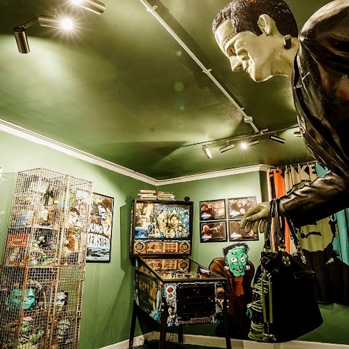 一个明亮的绿色房间,里面有与弗兰肯斯坦相关的物品,包括弹球机和大型怪物雕像