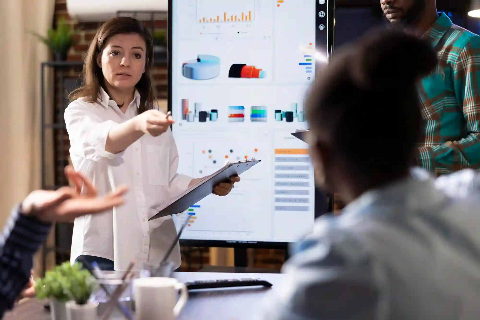 A confident female professional presenting data charts on a digital screen during a collaborative business strategy meeting.