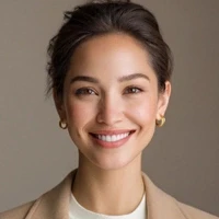A smiling woman in a beige blazer and white top, accessorized with gold earrings, against a neutral background.