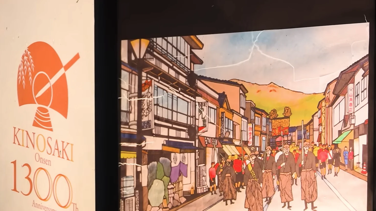 An illustrated panel marking Kinosaki Onsen's 1300th anniversary, showing bathers in yukata on the old street.