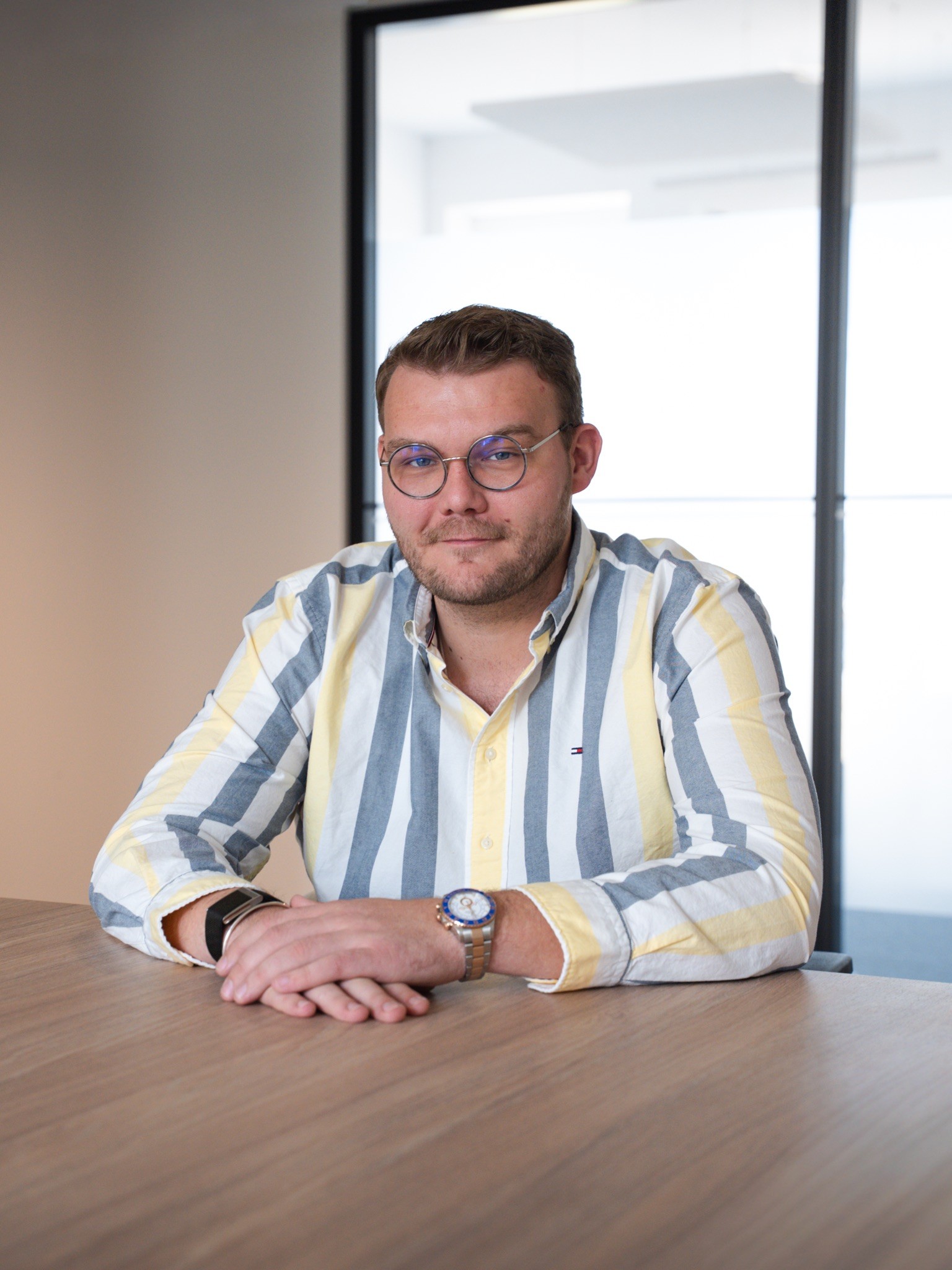 A young man with dark hair smiles at the camera, set against a modern indoor background.
