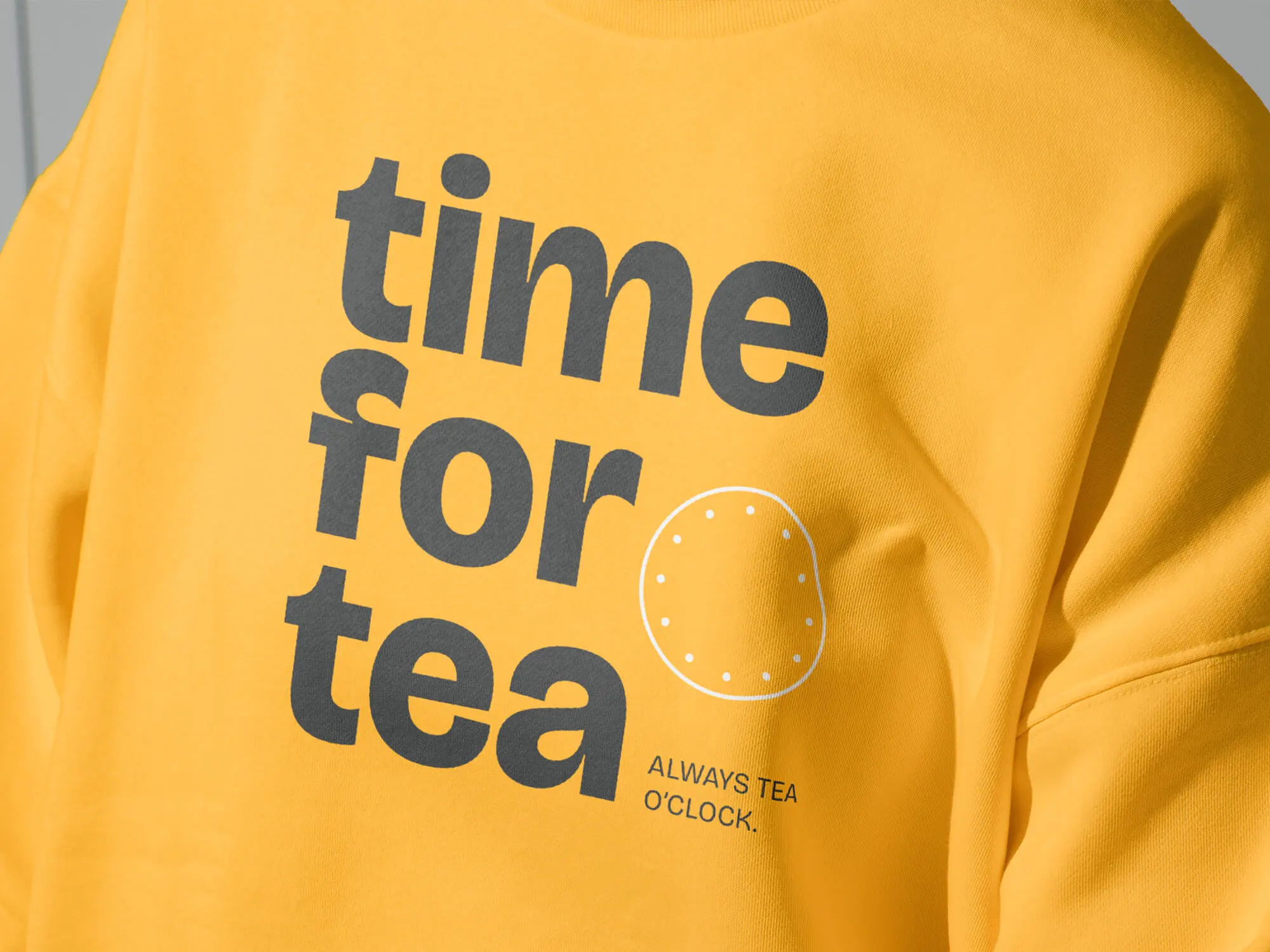 Närbild av en gul collegetröja med Time for Tea-logotypen, som lyfter fram varumärkets visuella identitet.