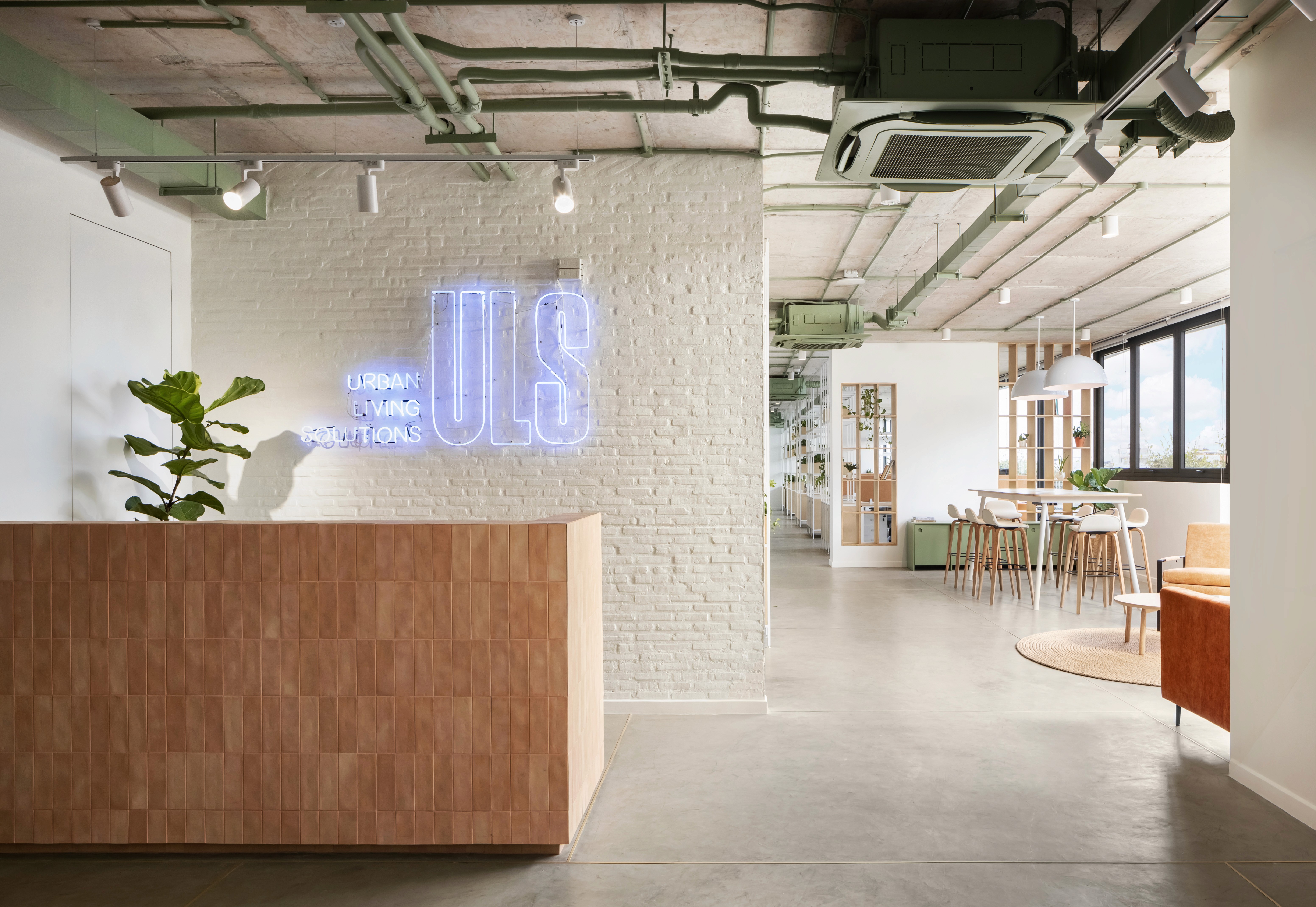 Interior design of a spacious open-plan office at ULS, featuring concrete floors, glass partitions, light wood furniture, and abundant greenery.