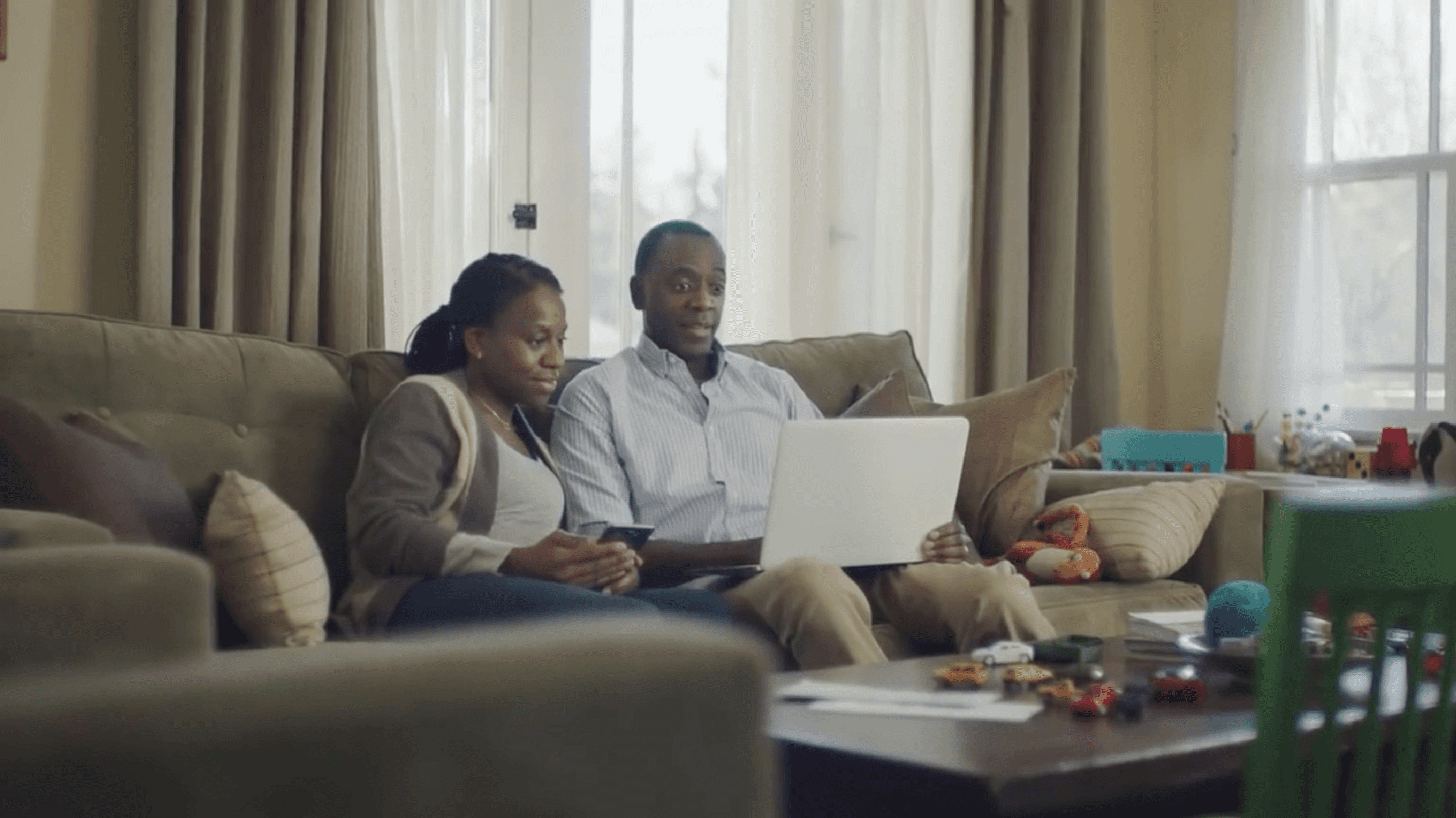 Two parents, a man and a woman, sitting on a couch looking at a laptop computer