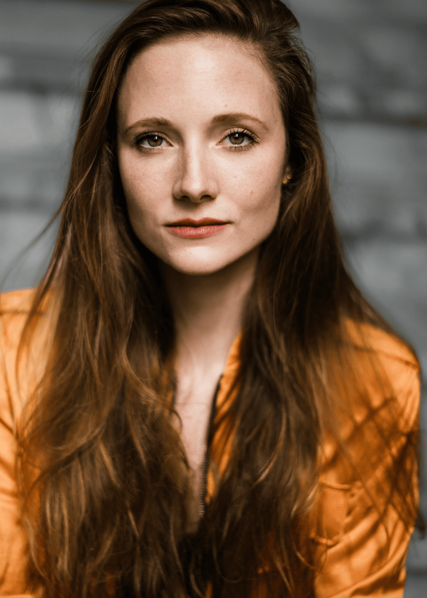 headshot casting photo of Joy Verberk, actor, woman with long brown hair, orange blouse, neutral background.