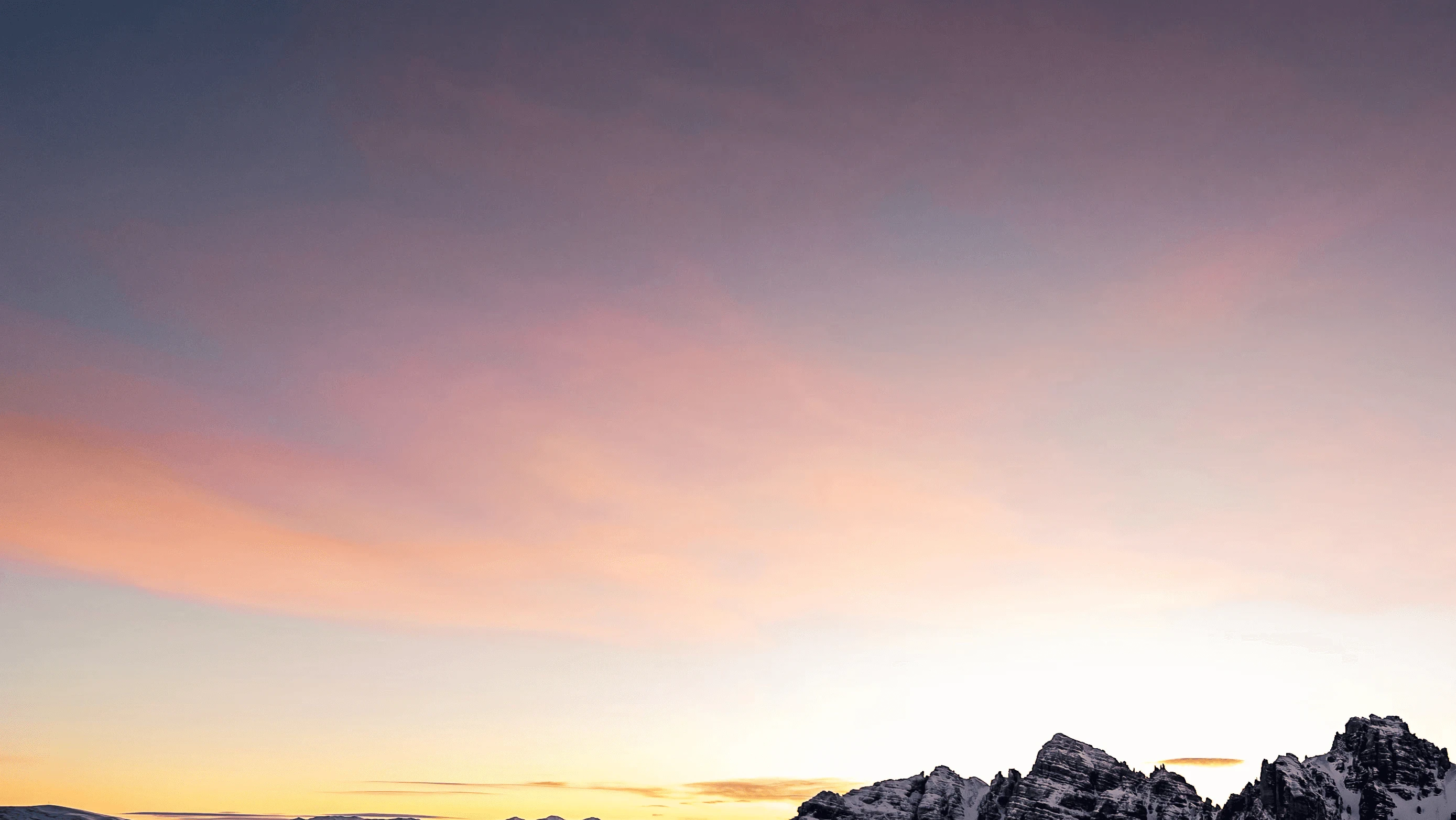 Ski resort sign with snowy mountain backdrop at sunset, promoting winter sports adventures.