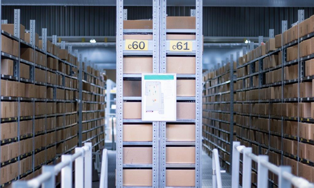 Fullpackade hyllor med bruna lådor i ett lagerutrymme. Märkta sektioner c60 och c61.