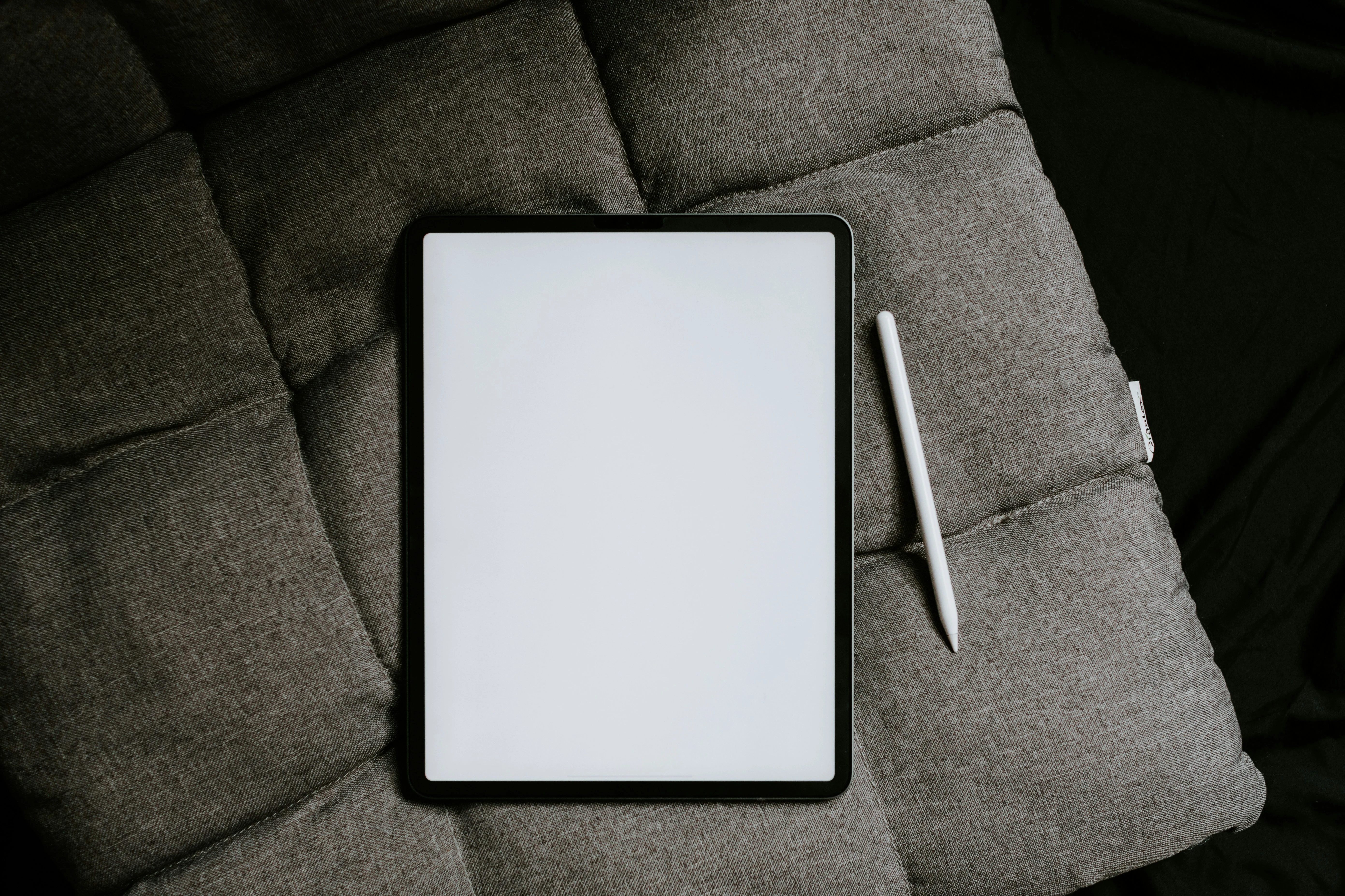 iPad with Apple Pencil placed on a dark gray cushioned surface, viewed from above.