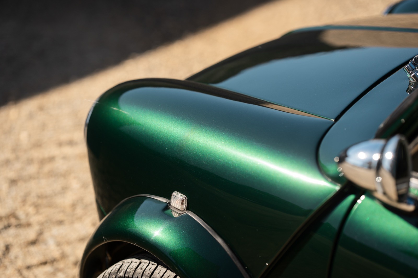 A small, green and black vehicle parked on a sandy surface, with a warm sunset lighting the scene.