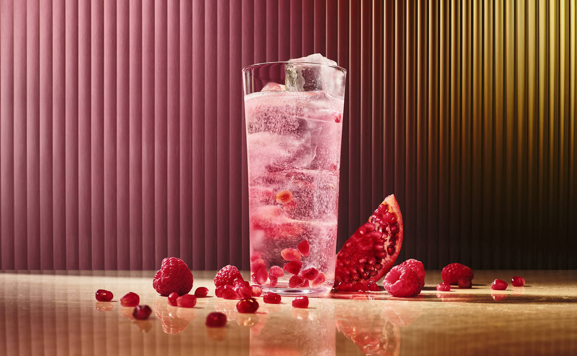 A refreshing pink drink garnished with berries, set against a colorful background. Berries scattered around the glass.