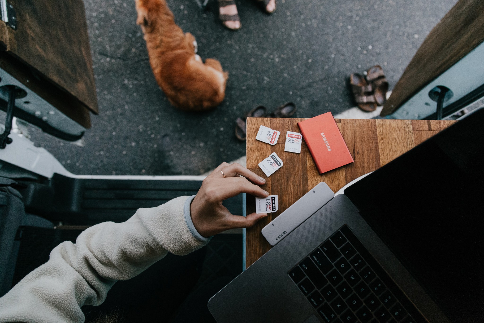 A person using SD cards and digital storage drives on a wood desk