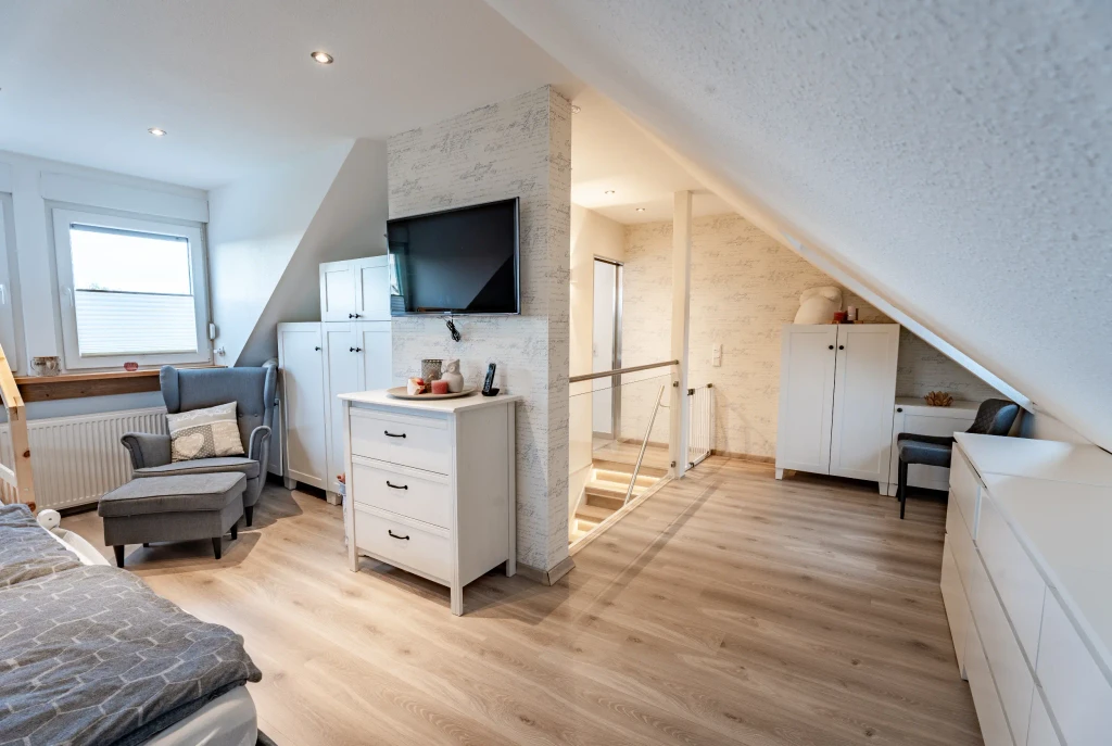 Gemütliches Dachgeschosszimmer mit Fernseher, Sitzbereich und heller Einrichtung in einem Einfamilienhaus in Gronau – Westfalen Wohnen.