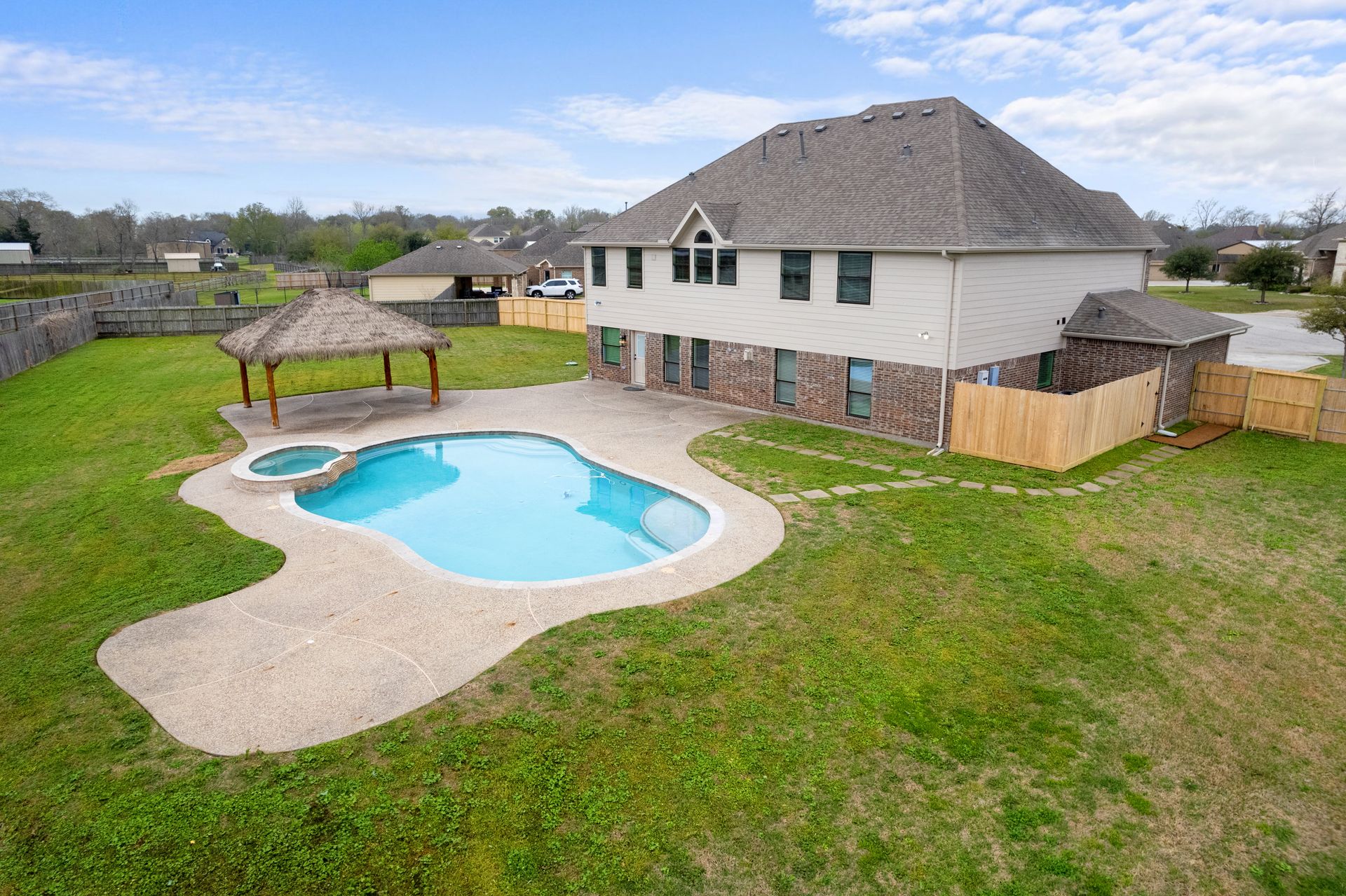 Aerial drone photo of a two-story home with a pool, spa and palapa on a large lot