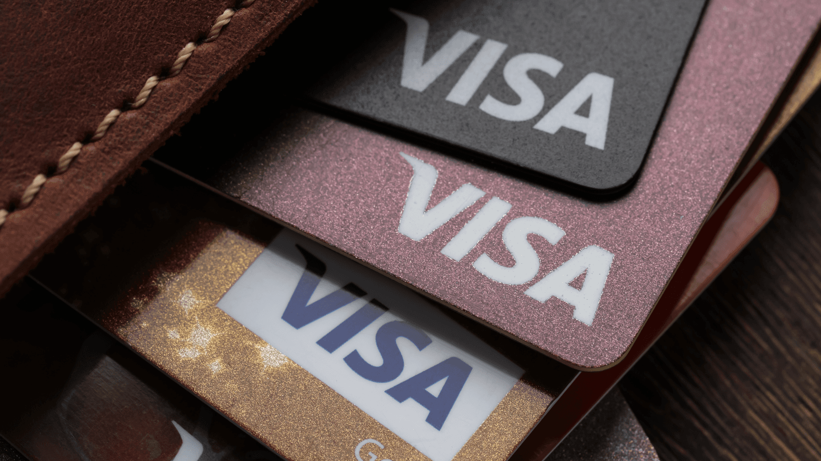 Visa-Karten in Schwarz, Rosé und Gold ragen aus einer Ledergeldbörse, als Auftakt zu Tipps für die VAMP-Änderungen.