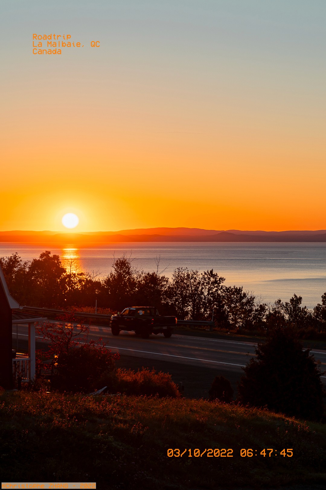 Route au lever du soleil à La Malbaie, avec le fleuve Saint-Laurent en arrière-plan.