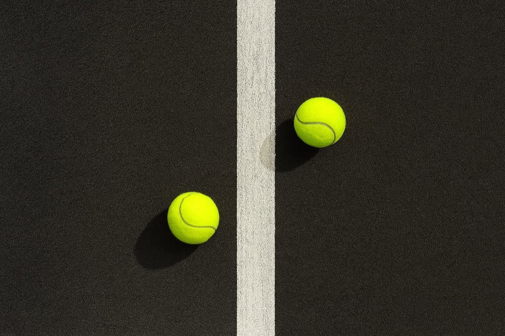 Zwei gelbe Padelbälle liegen auf der weissen Mittellinie eines schwarzen Courts – schlichtes Detailbild mit Fokus auf Präzision und Design bei Padelnero.