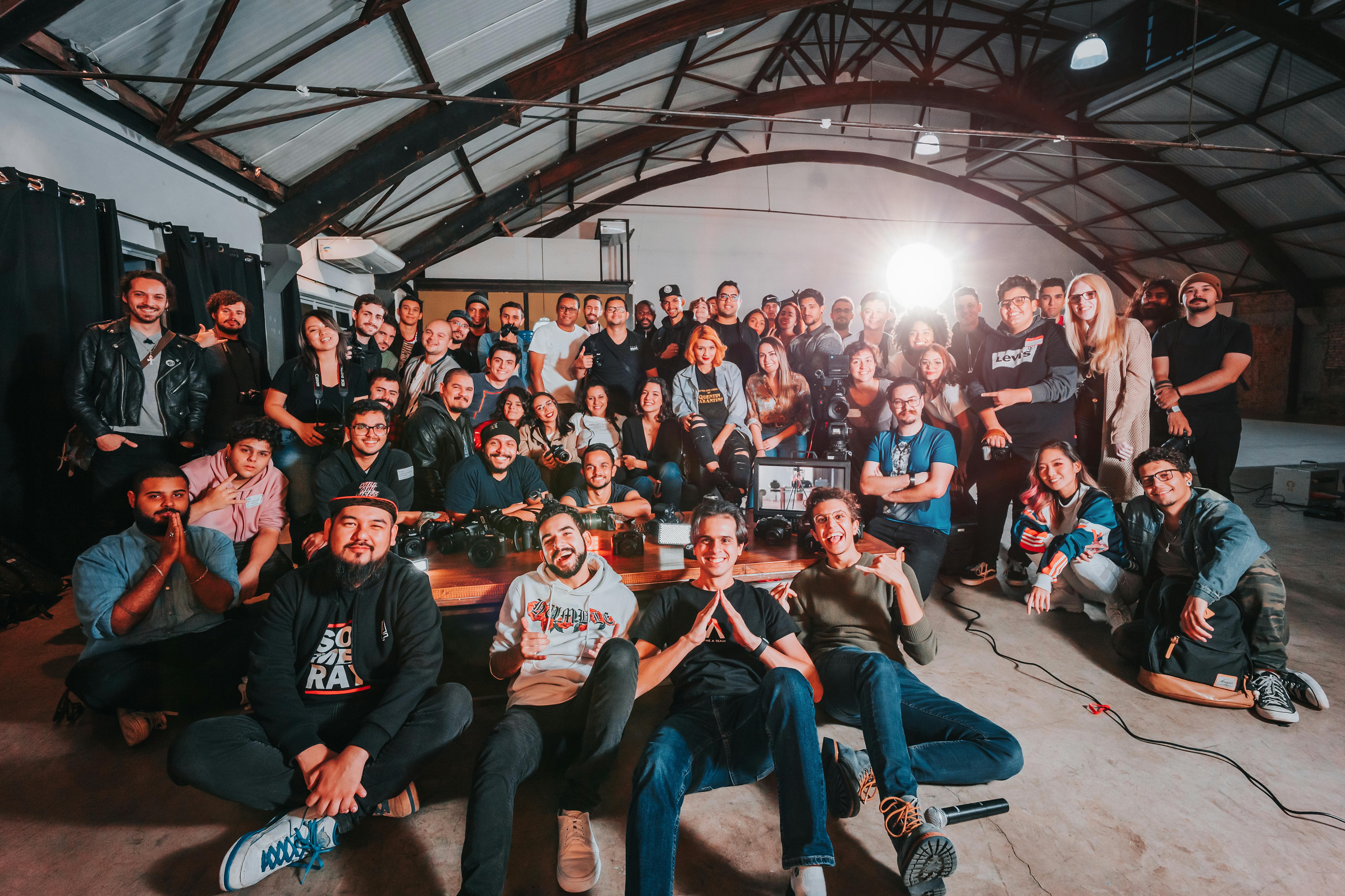 Un grande gruppo di giovani professionisti e creativi riuniti in uno spazio industriale moderno, simbolo di collaborazione, crescita e formazione condivisa.