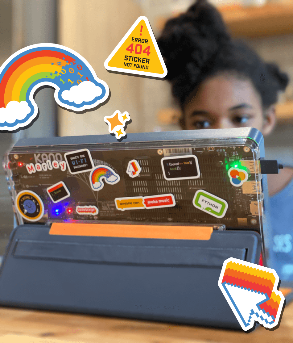 A 2-in-1 tablet sits on a table. The back of the laptop is clear, showing the circuit board beneath. On the cover there are several stickers, including a computer curson with a rainbow trail, and other references to coding and computers.