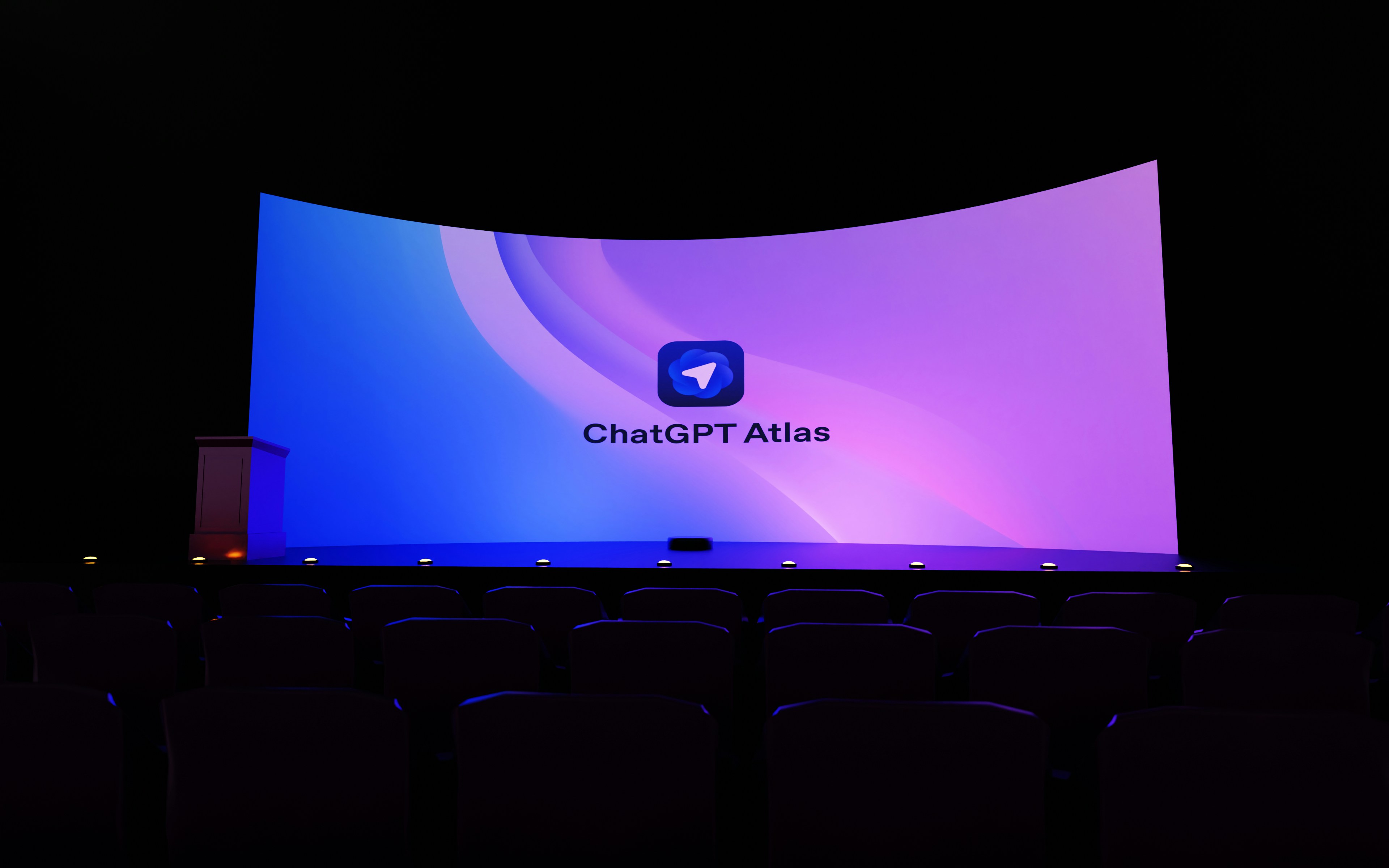 A large screen displays "chatgpt atlas" in a dark room.