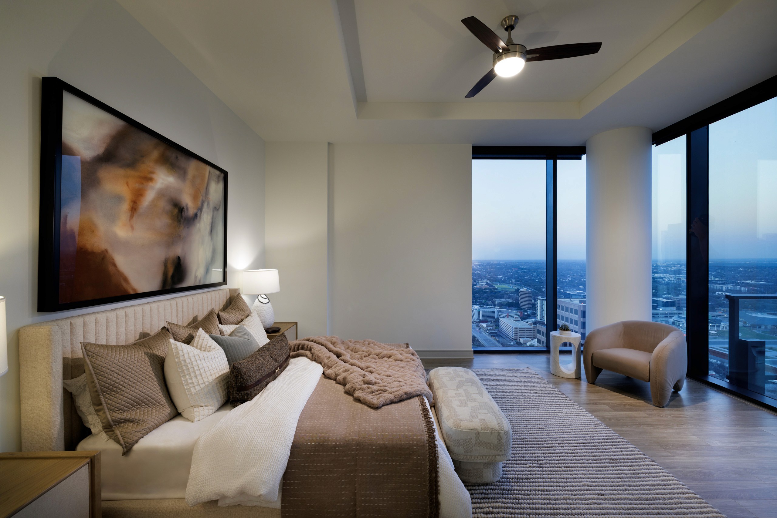 Bedroom with city view, large artwork, and tufted bed.