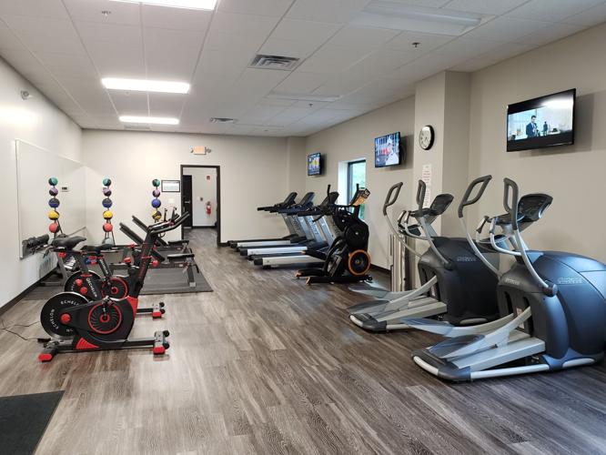 A clean gym interior with exercise machines, weights, and a TV on the wall, featuring wooden flooring.