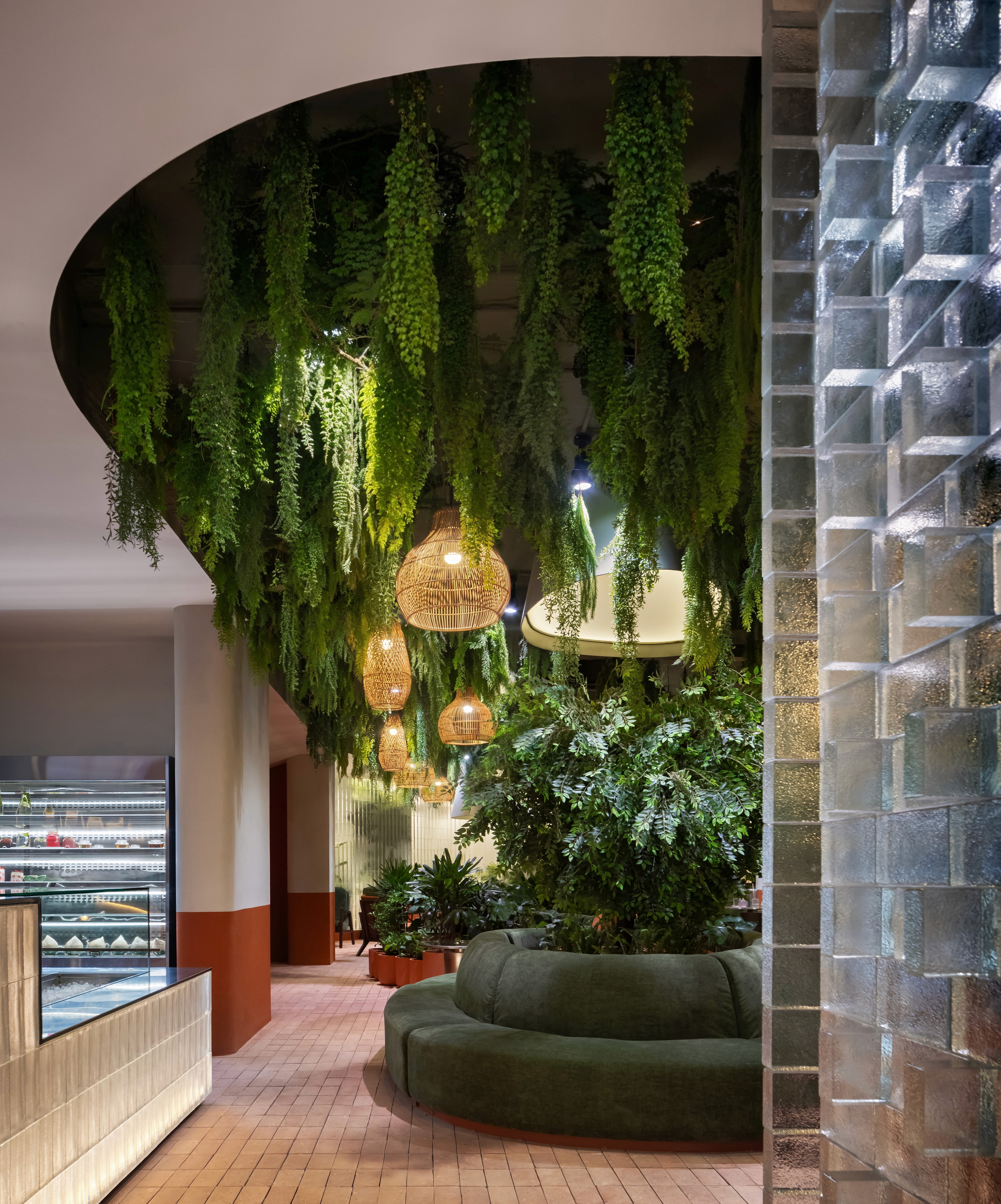 Interior planted ceiling with rattan pendant lighting above lounge seating, central biophilic spine and warm ambient illumination encouraging longer dwell times and wellbeing
