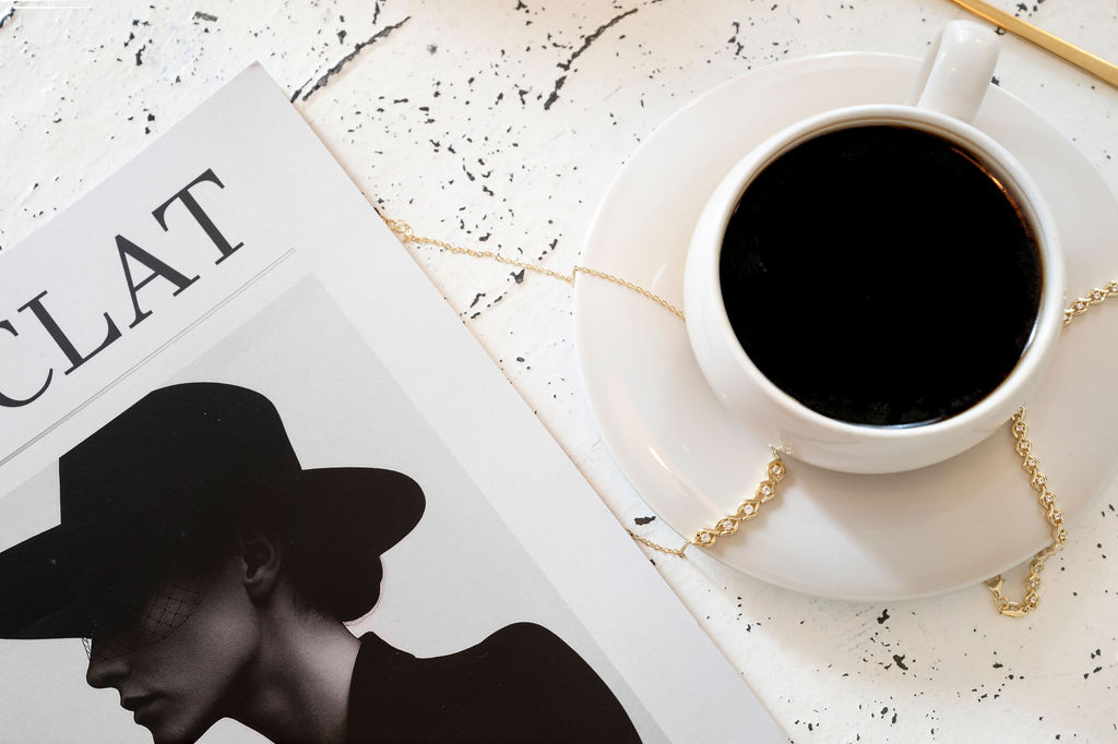 editorial style photography featuring a chic french magazine, and a cup of coffee with gold tennis bracelets placed around the saucer