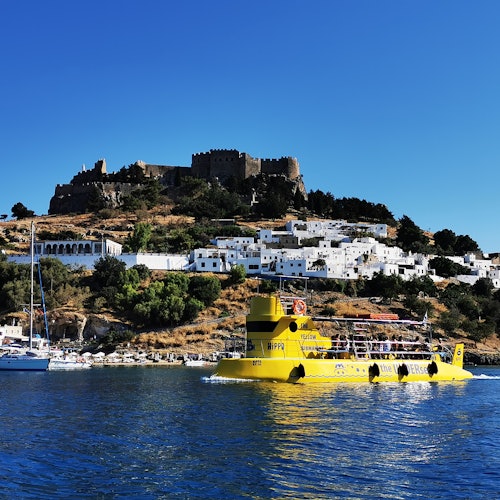 Giallo intenso, una barca sulle acque con una cittadina collinare e un castello storico sullo sfondo, sotto un cielo azzurro.