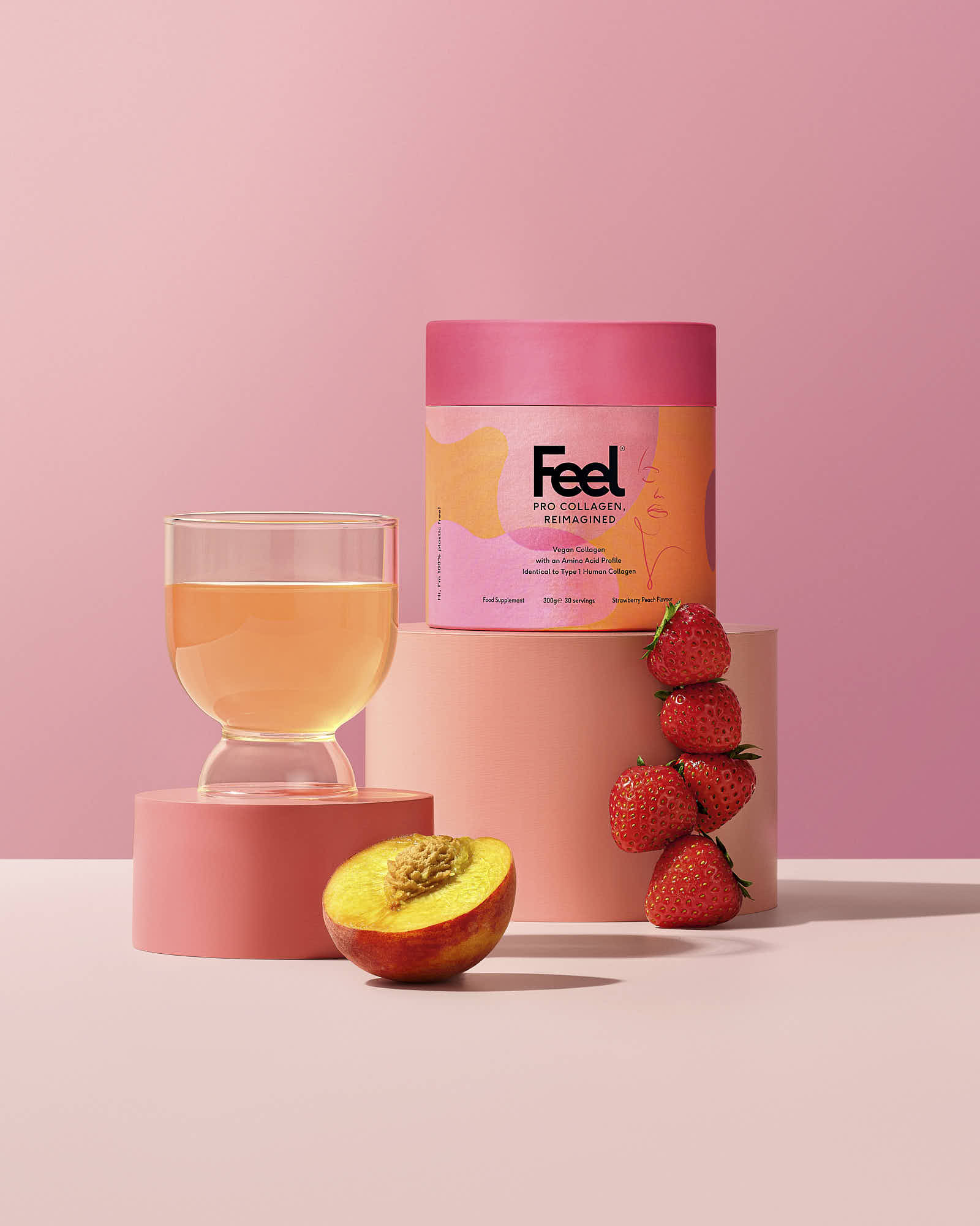 A pink-themed display featuring a canister, glass of drink, and peach, set against a soft pink background.