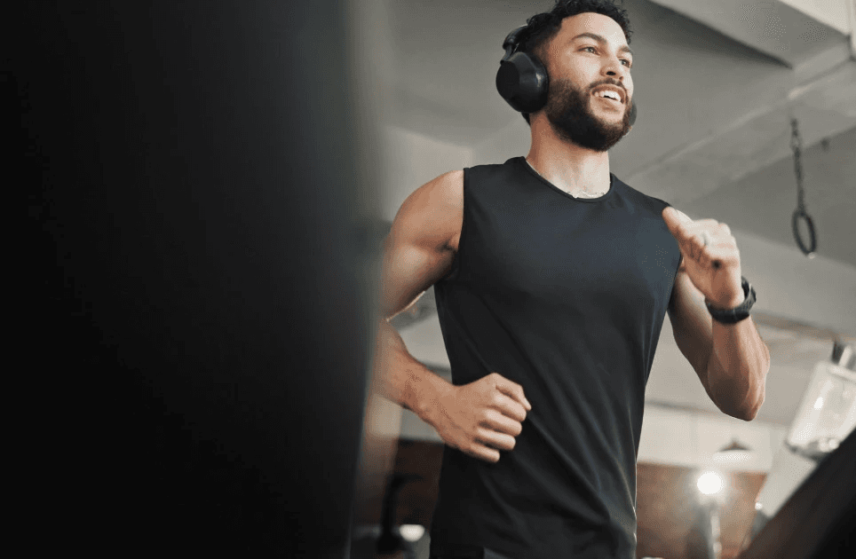Man with headphones running on a treadmill in a gym, focused on his cardio workout.