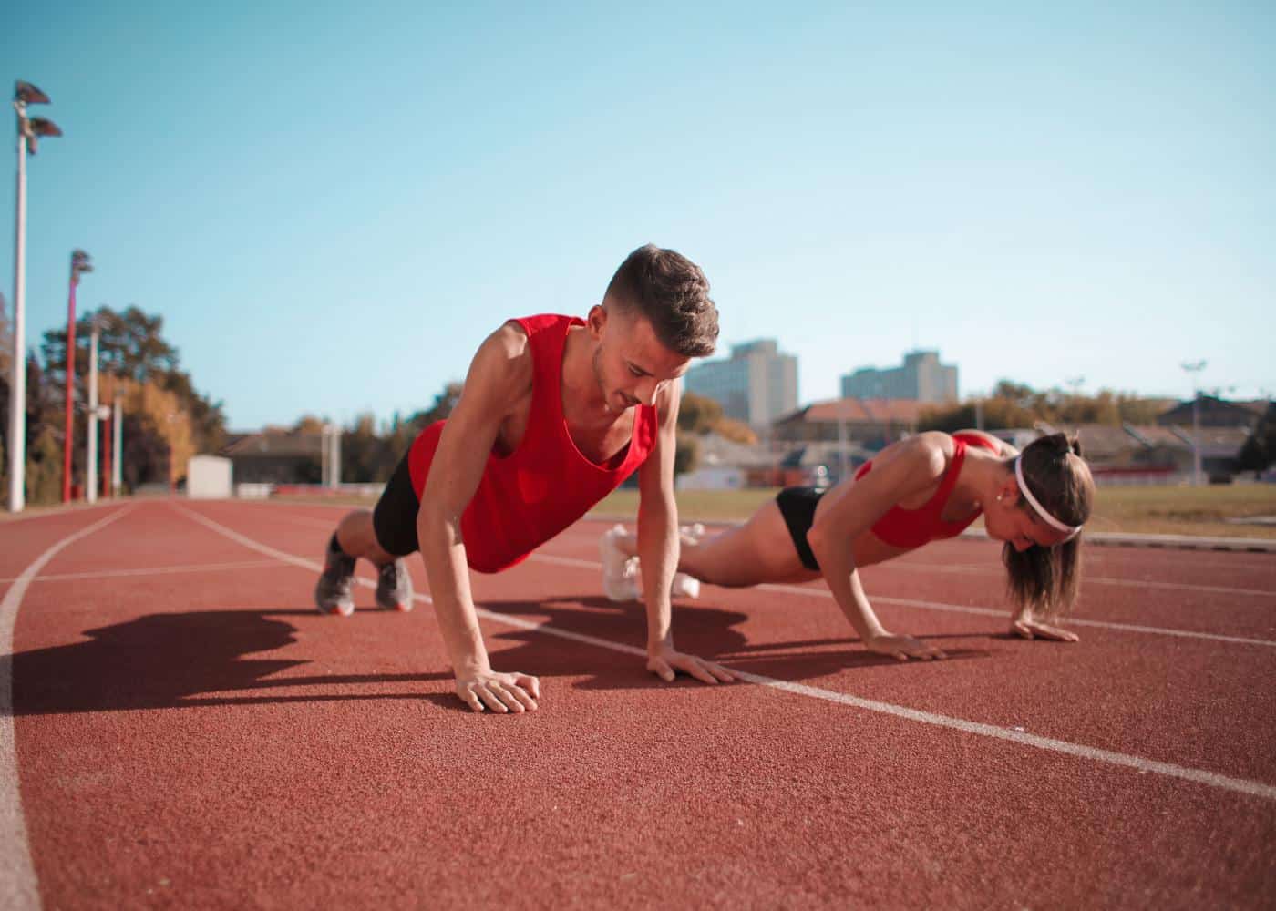 Man and woman performing pushups on a race track.