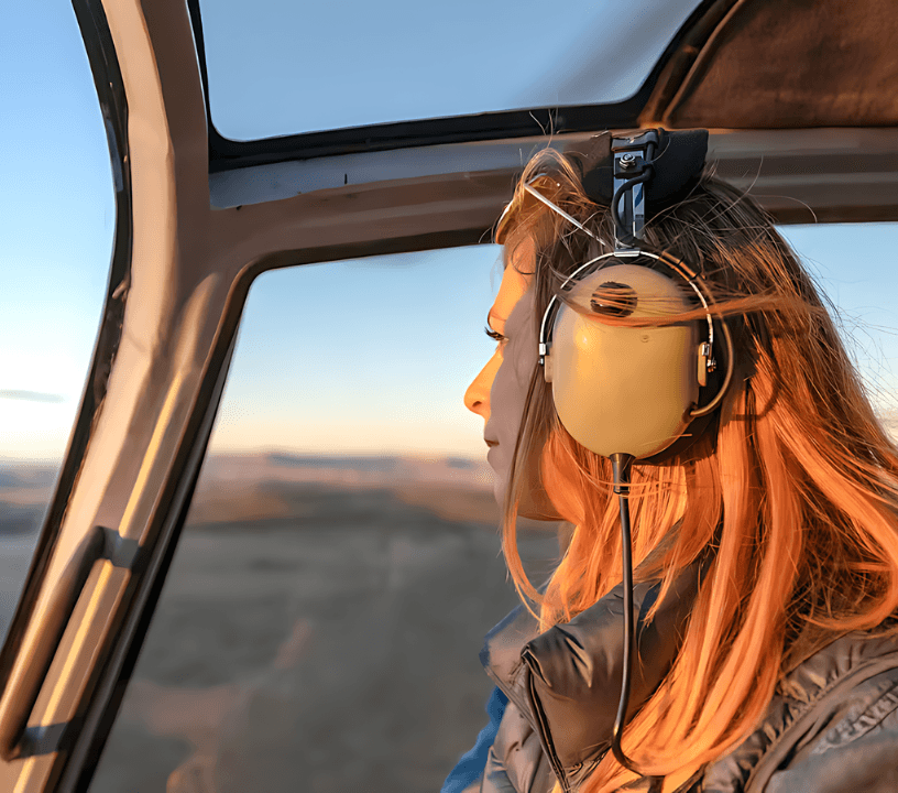 A women is sitting in a helicopter cabin, wearing headphone and looking out to Grand Canyon view