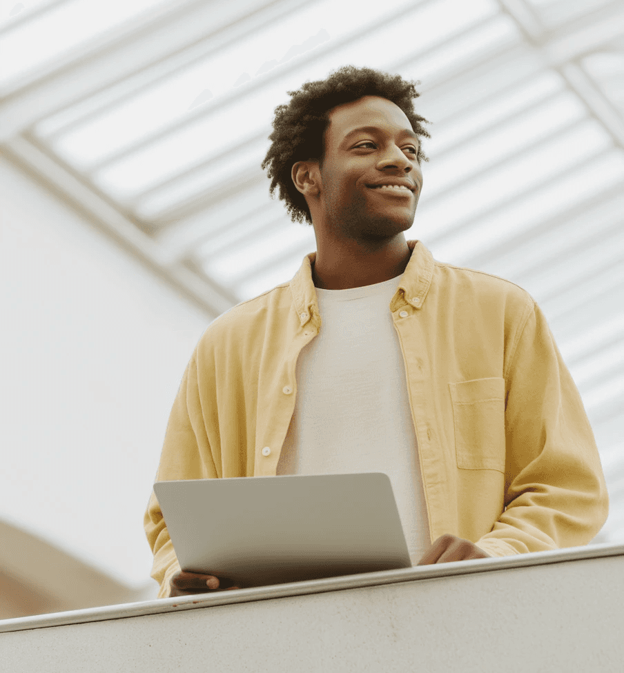 Smiling young man in yellow shirt holding laptop