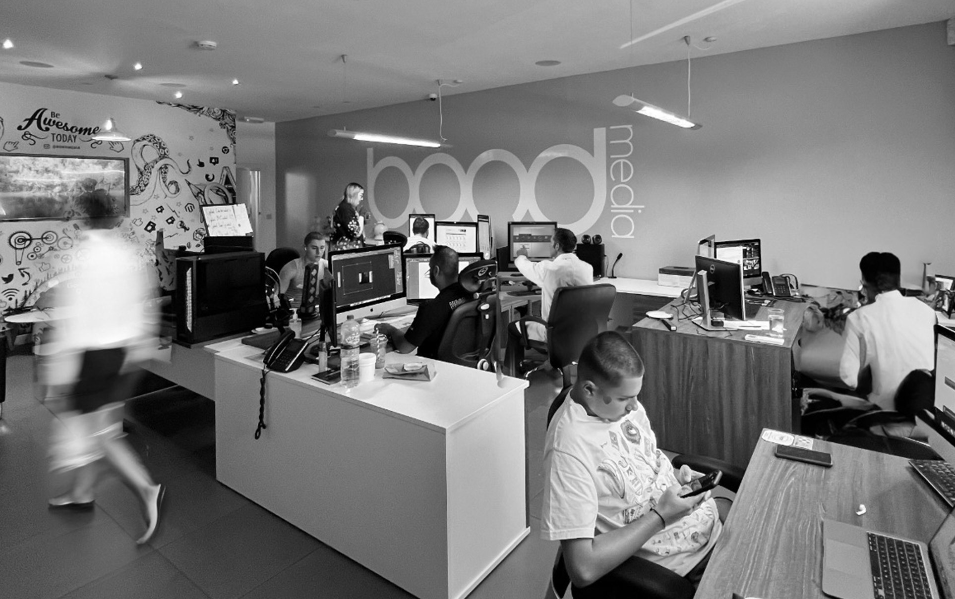Black and white image of people working at a table with laptops, showing hands gesturing during discussion of digital content displayed on screens, with fabrica® logo in the corner.