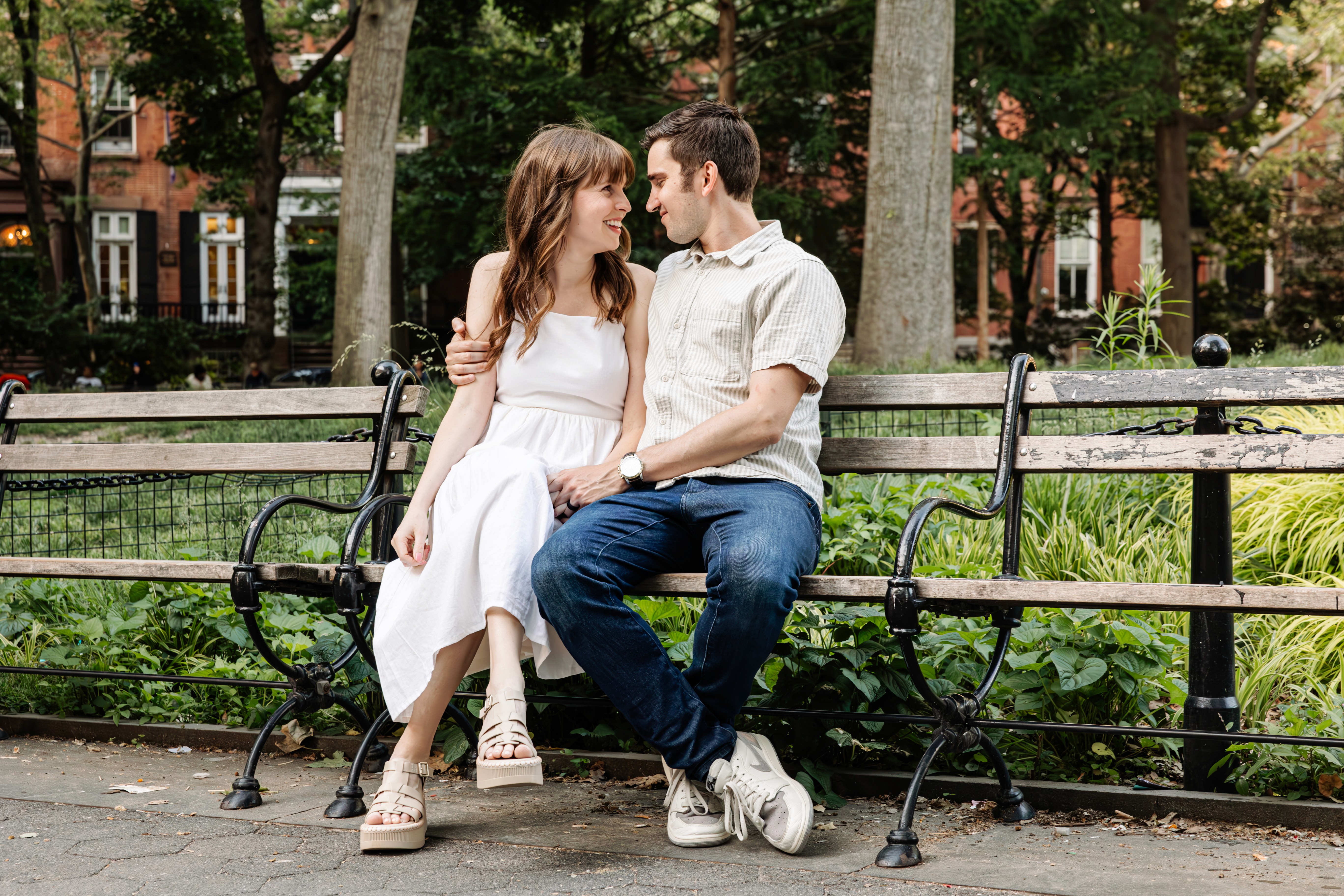 Newly engaged couple sharing a quiet, loving look on a bench in Washington Square Park, NYC — she's radiant in a white dress — romantic engagement photography by Lizz Spano Photography, New York City engagement photographer.