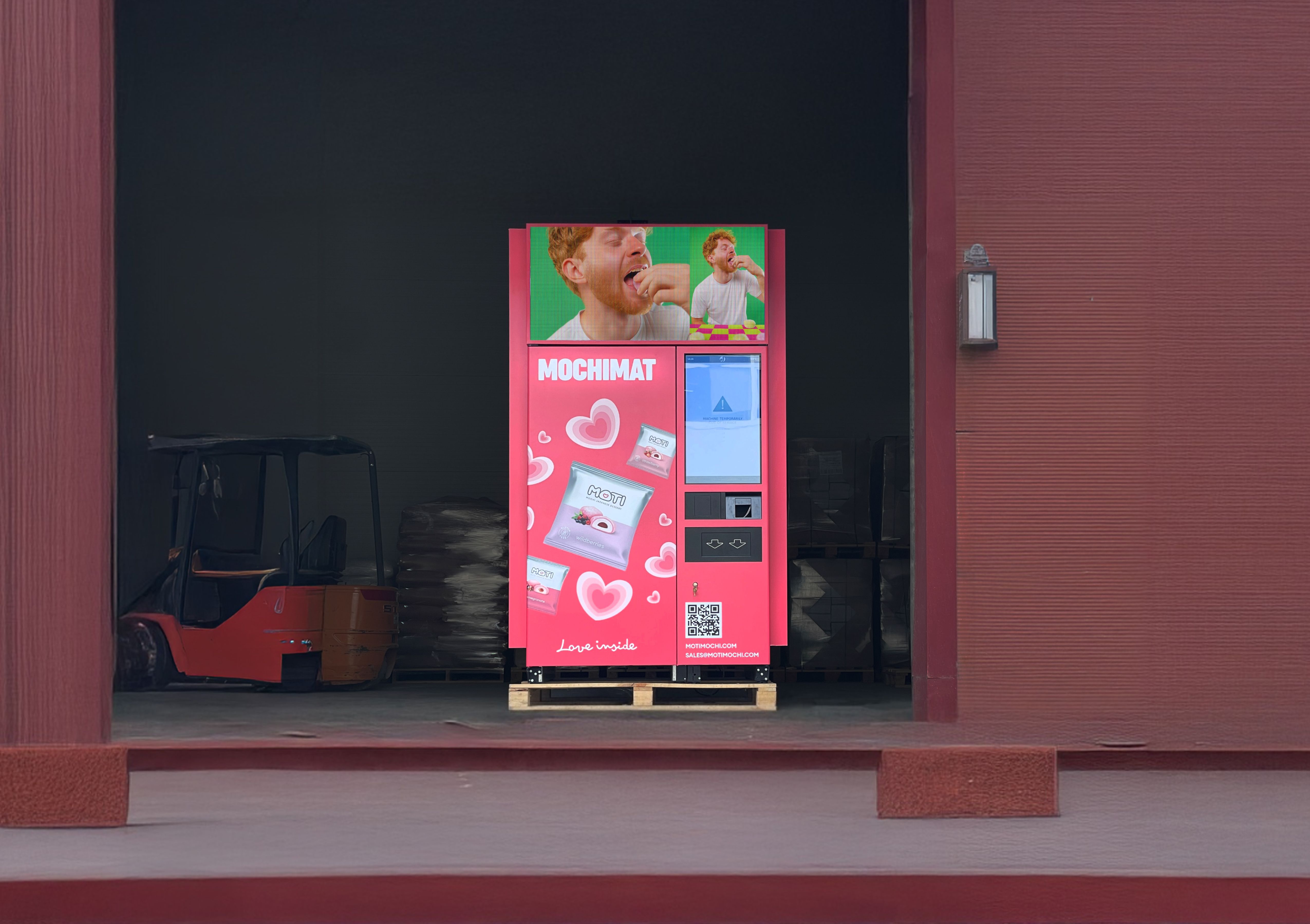 Bright pink MOCHIMAT vending machine branded with MOTI desserts and the slogan “Love inside,” placed inside a warehouse setting.