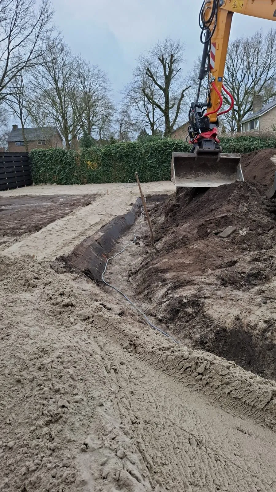 Graafwerkzaamheden met een graafmachine in een kale nieuwbouwtuin in Lippenhuizen, voorbereiding voor kindvriendelijke familietuin.