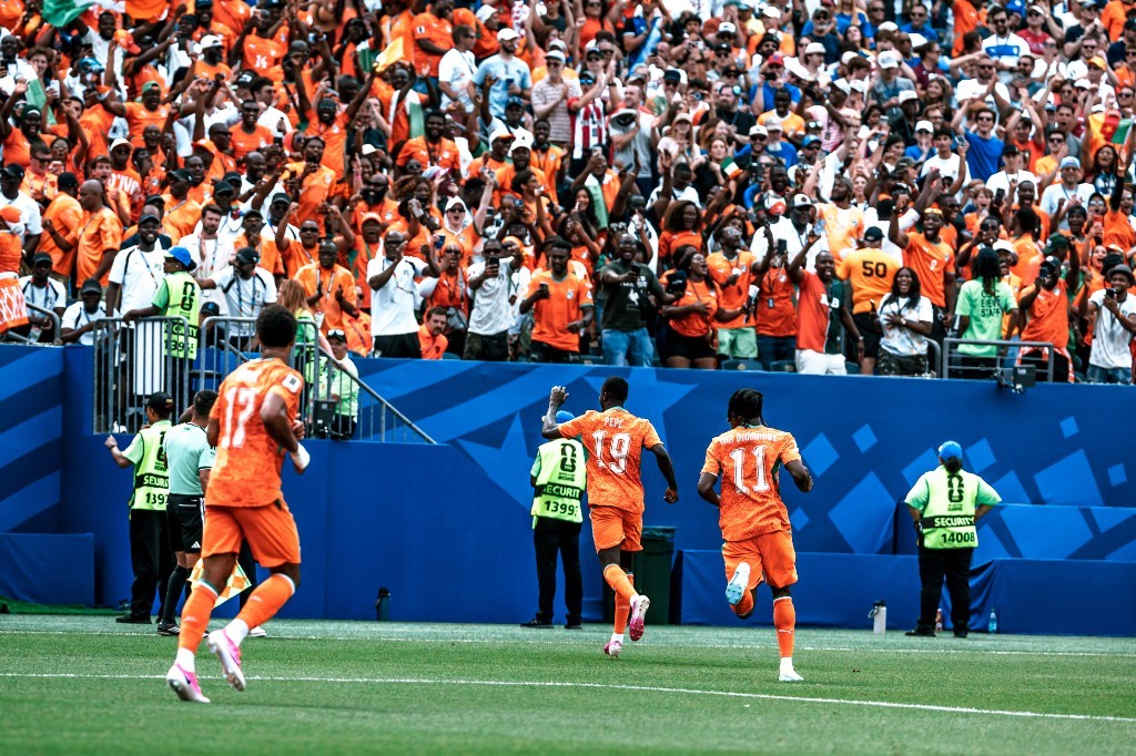 Nicolas Pépé, Yan Diomande, and an Ivory Coast teammate run toward a sea of orange fans after a goal in Philadelphia