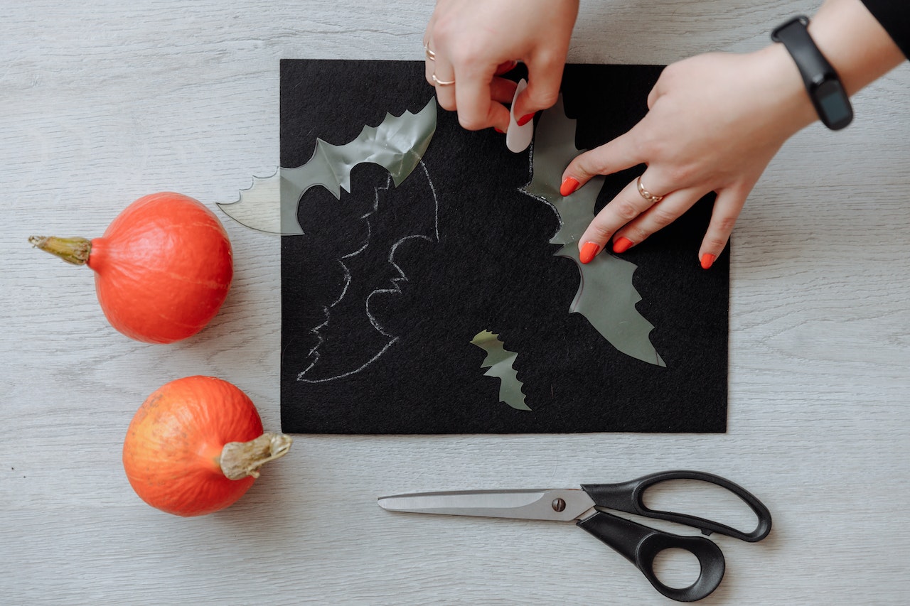 A persons hands tracing around a bat shape onto a piece of black card
