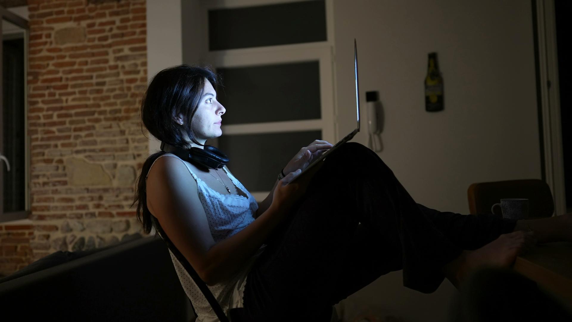 Woman working at night at home in front of laptop computer in the dark