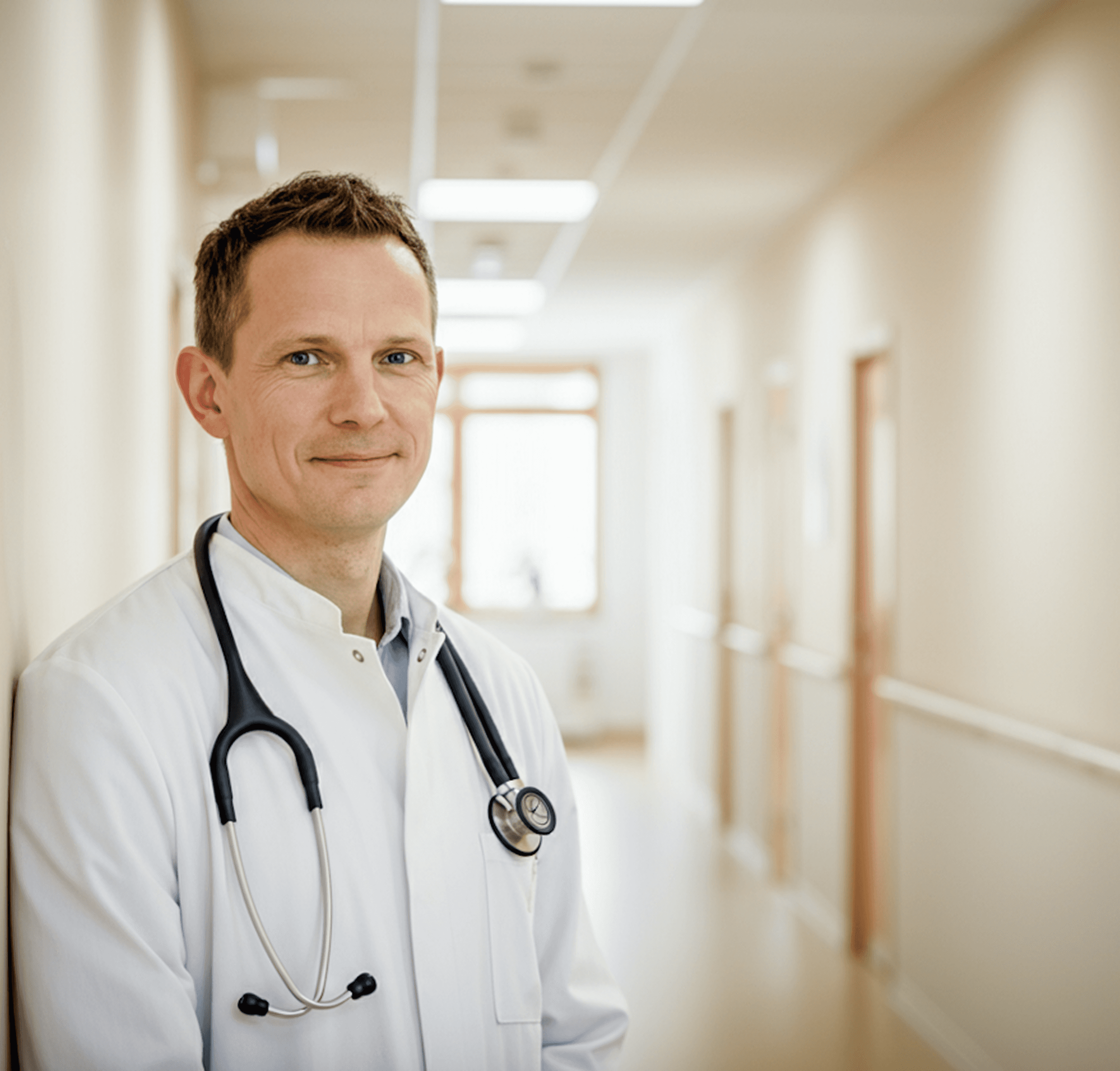 Doctor in white coat with stethoscope standing in bright hallway of healthcare facility