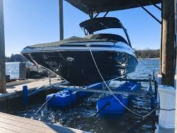 A sleek black and white speedboat is elevated on a blue boat lift at a dock, surrounded by calm waters under a clear blue sky.