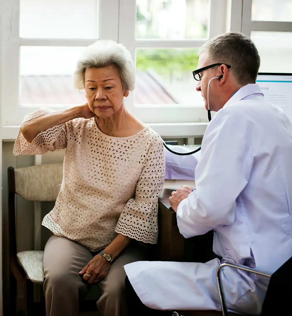 Older woman with health anxiety looking concerned while a doctor examines her with a stethoscope
