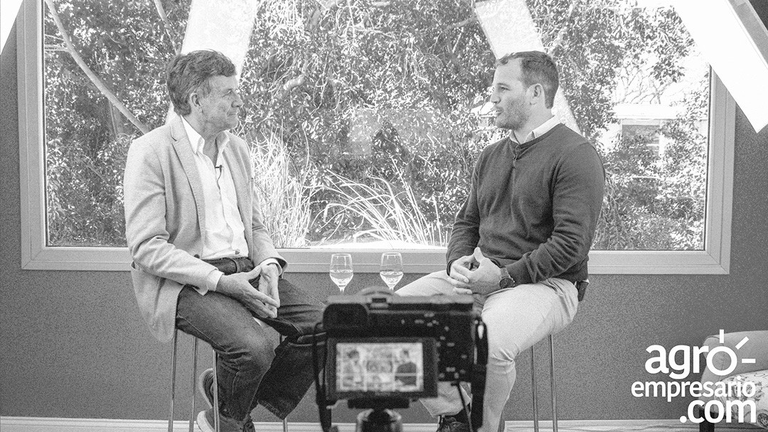 Two individuals seated in front of a large window during a recorded interview.