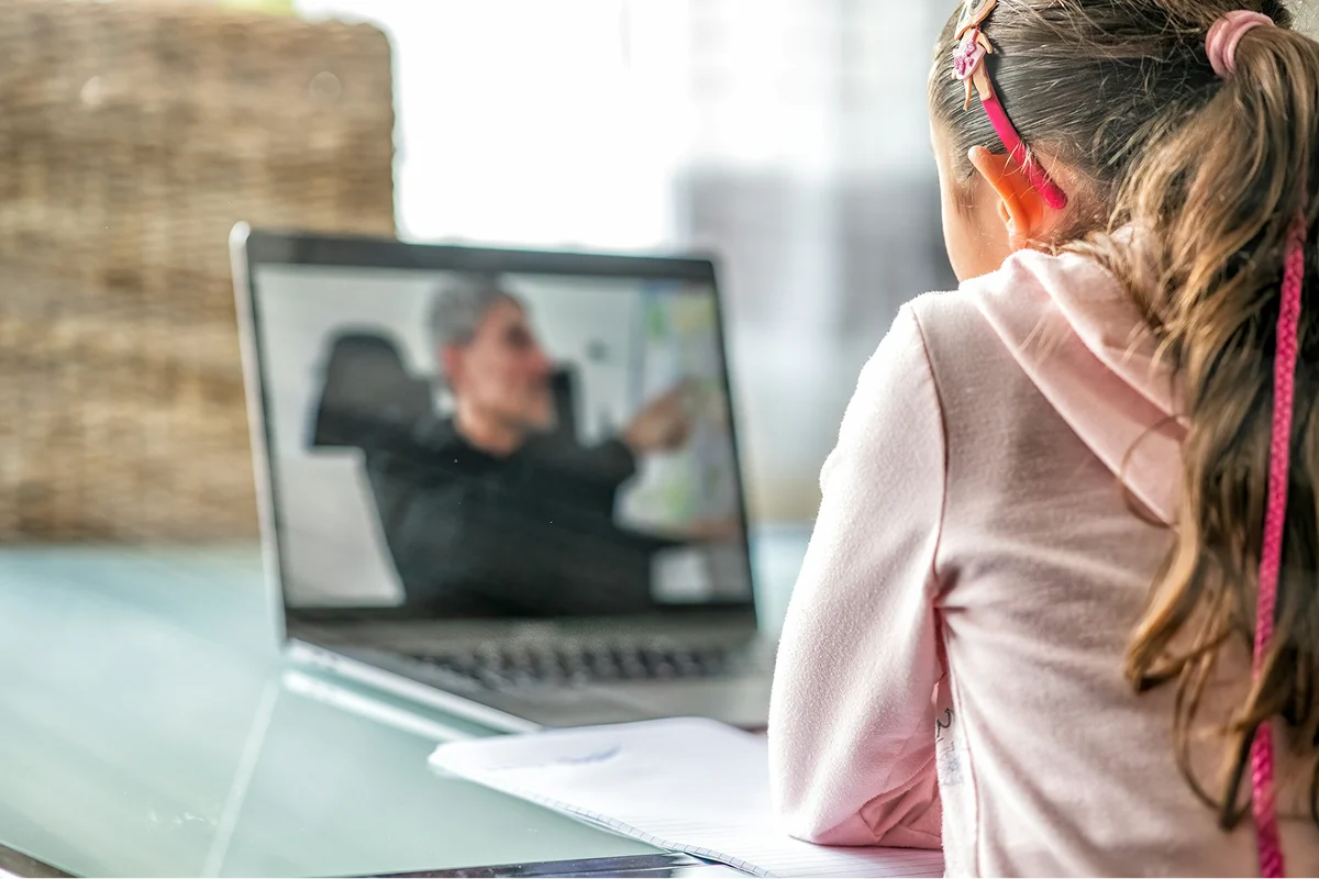 A girl wearing headphones and speaking with someone on a laptop.