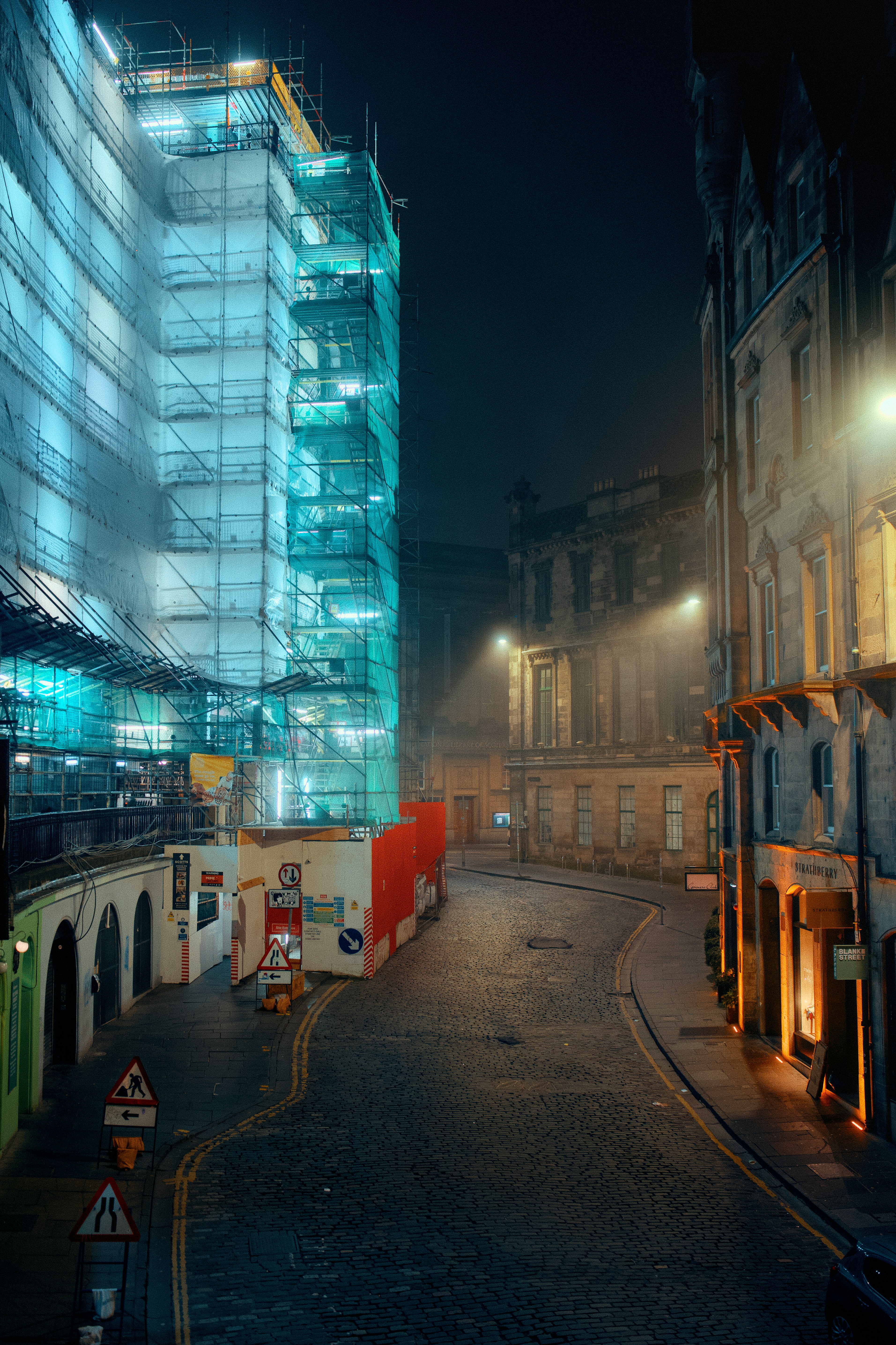 Scaffolding covers building under construction at night.