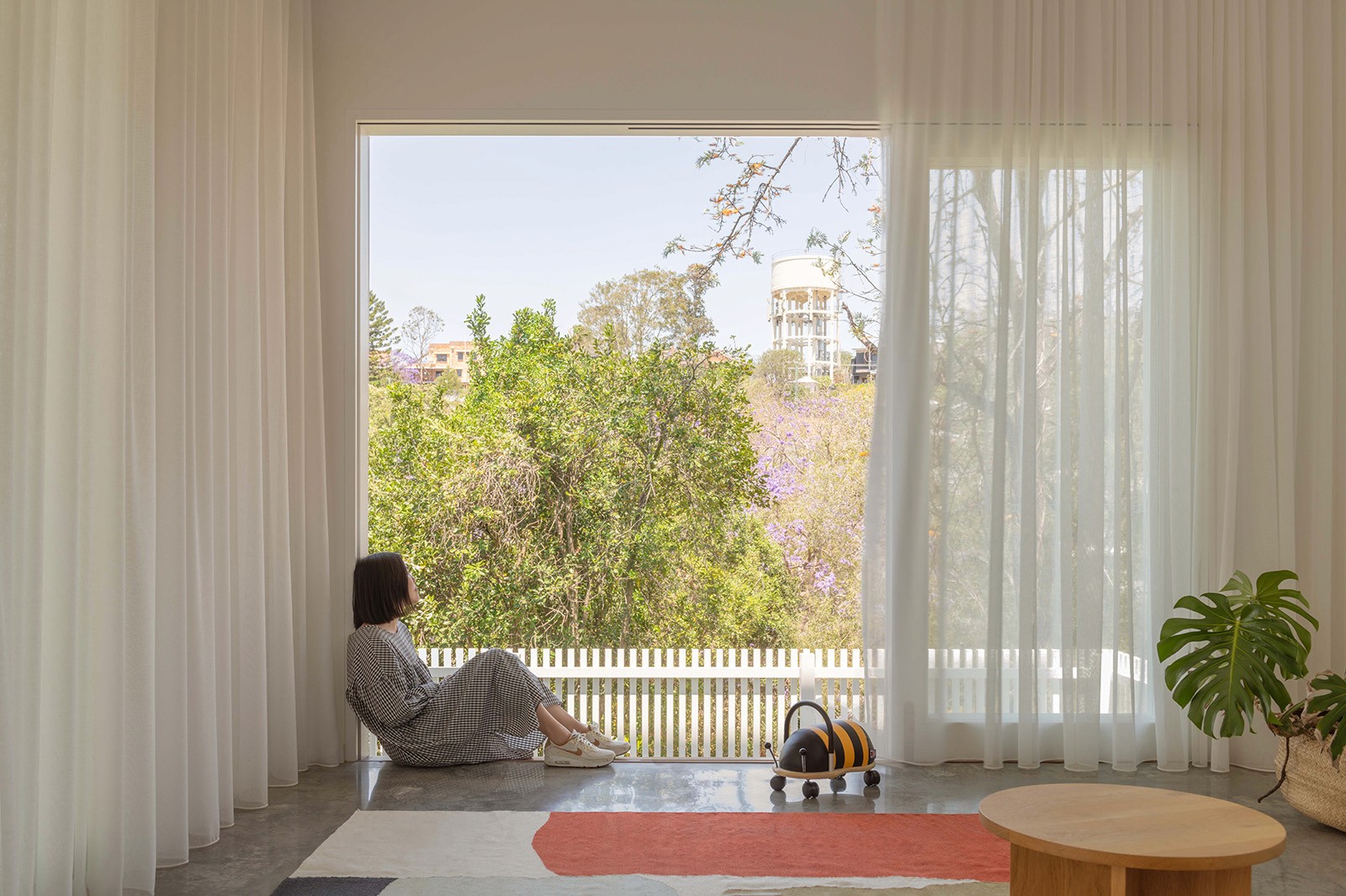 Quiet sitting nook with full-height window, sheer curtains, and leafy suburban views beyond.