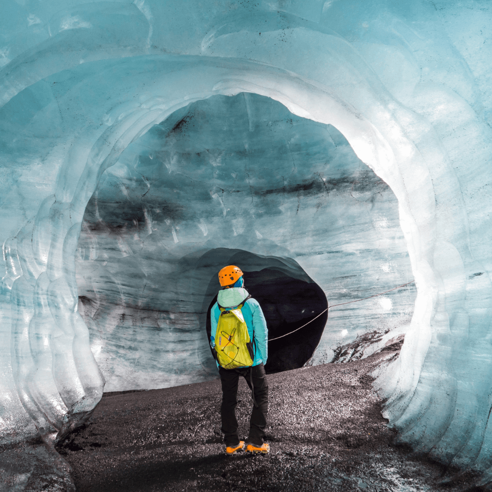 Person exploring Katla ice cave in Iceland near Vík, standing inside blue glacier tunnel with volcanic ash layers, a popular South Coast glacier and ice cave tour experience.