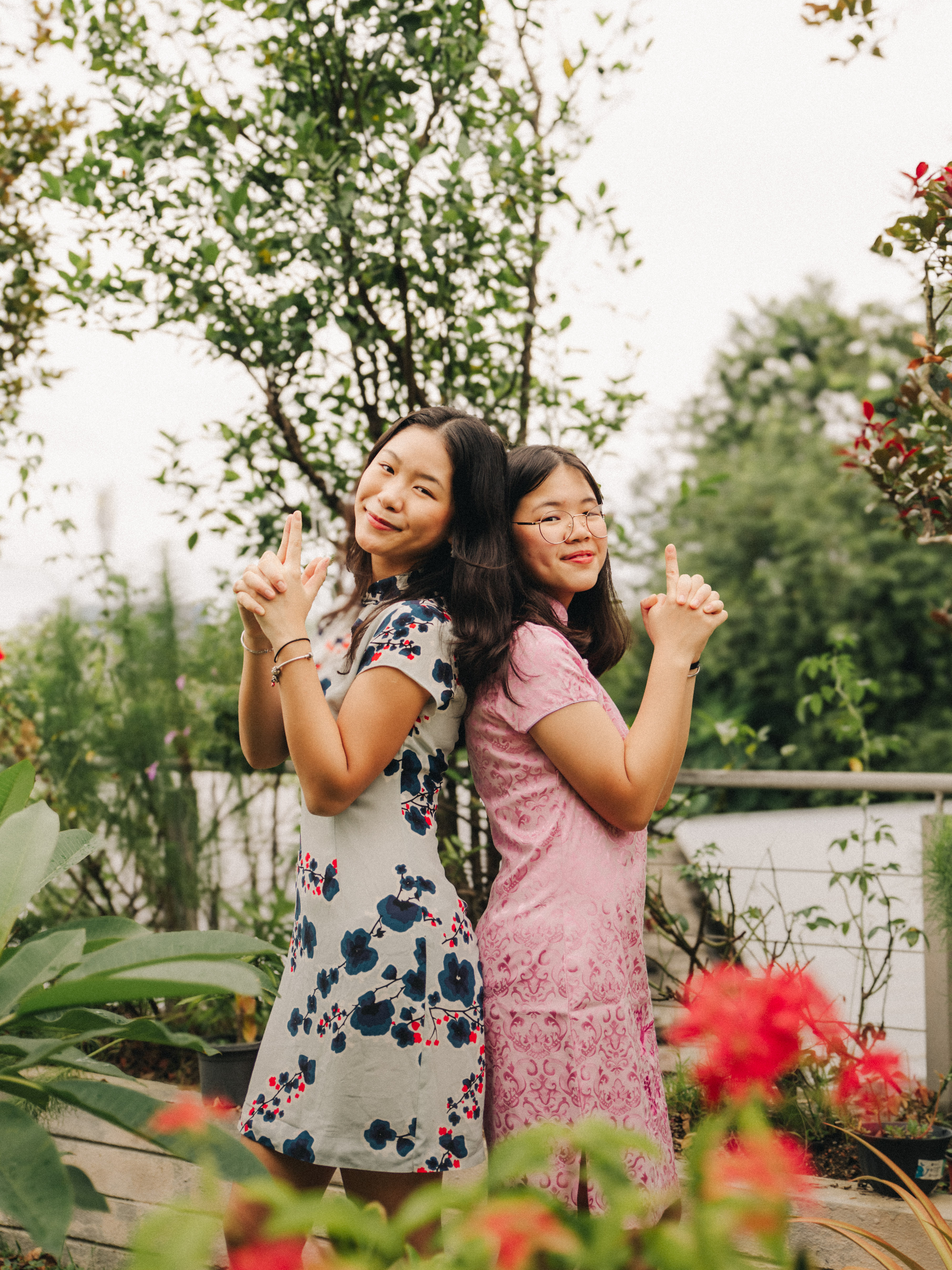 Sisters posing for a festive CNY photo amidst the vibrant flowers of a garden