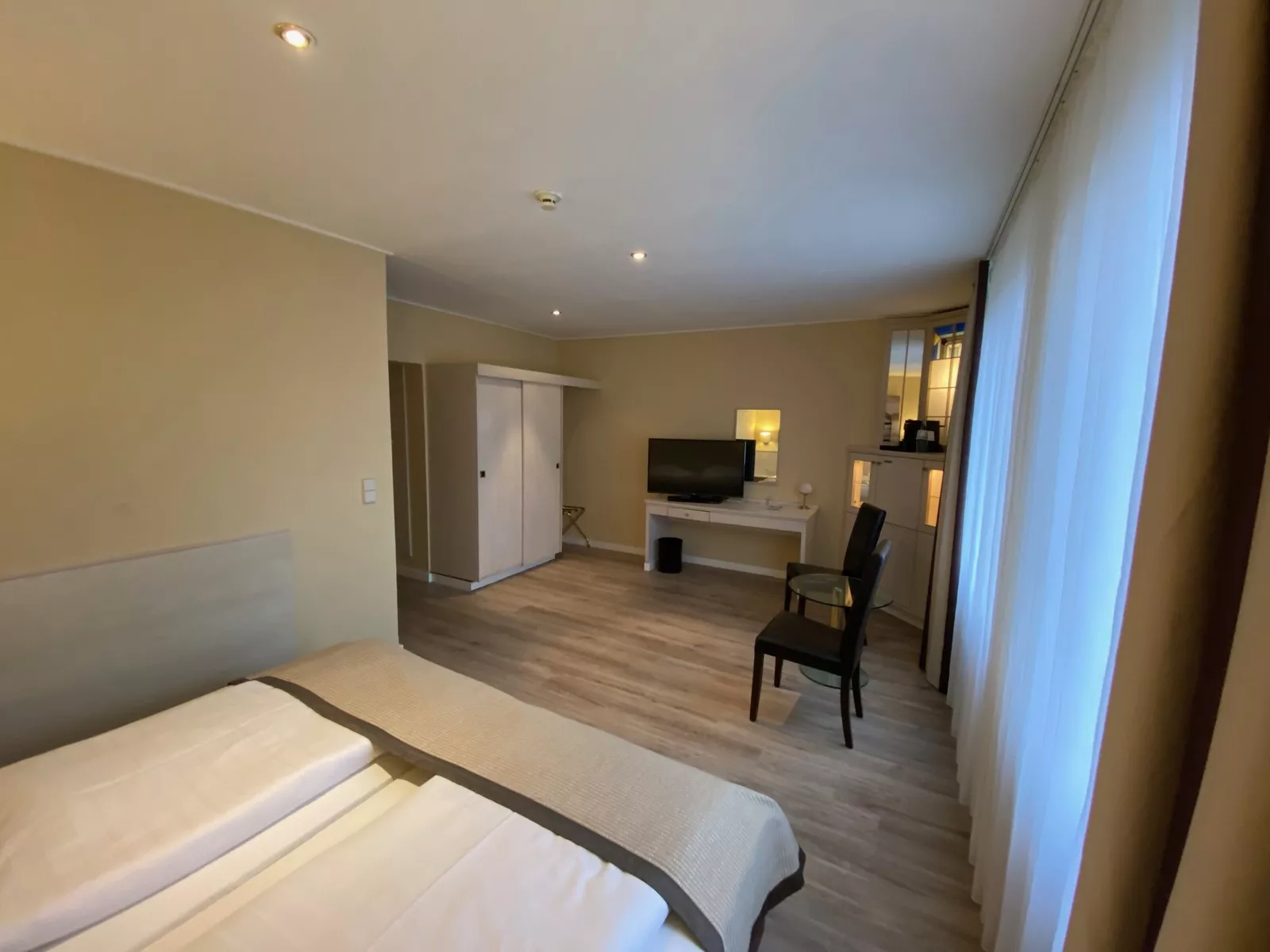 Bild vom Comfort Zimmer vom Bett aus fotografiert mit Blick auf einen Schrank, TV, sowie Sitzecke mit zwei Stühlen